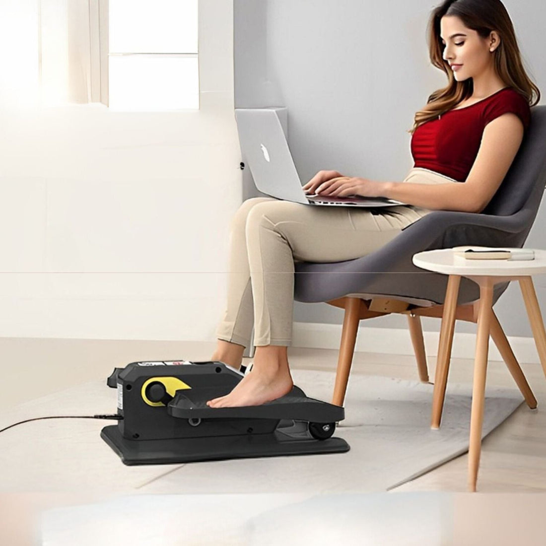 Young female professional using a motorized under-desk elliptical while working on a laptop to prevent health debt and improve leg circulation
