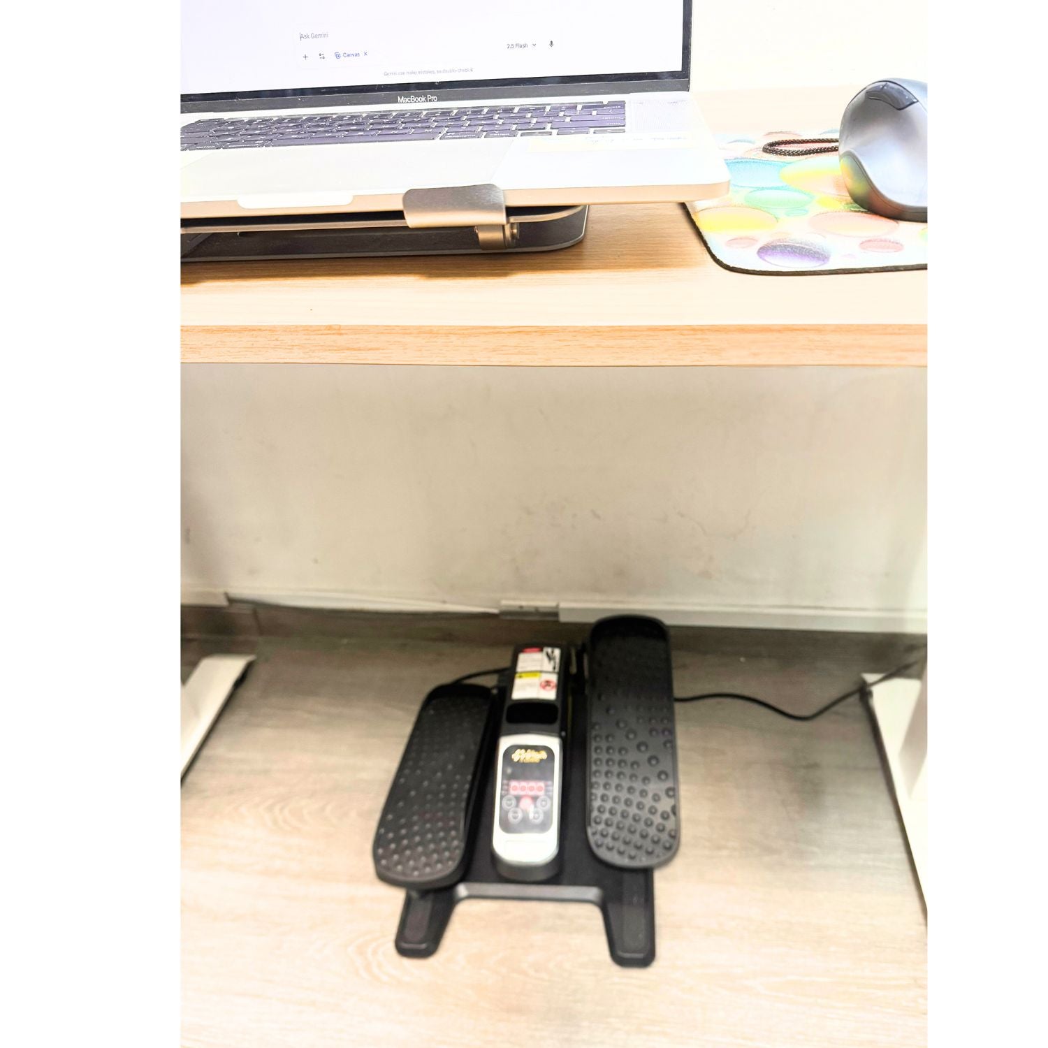 Mini Elliptical Trainer perfectly fitting under a standing office desk in a home environment. Demonstrates compact size and discreet usage